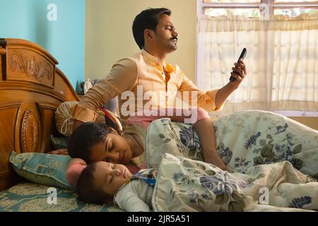 Father using Smartphone while mother and baby sleeping on bed in the morning Stock Photo