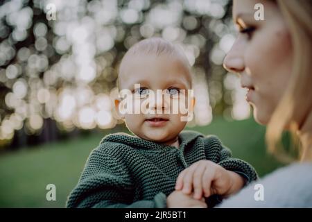 Mother holding her little baby son wearing knitted sweater during walk in nature. Stock Photo
