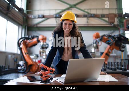 Portrait of female chief engineer in modern industrial factory using computer. Stock Photo