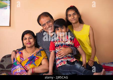 Portrait of lower middle class family sitting together on cot in the ...
