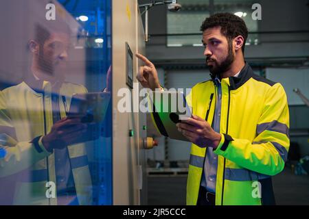 Young industrial worker operating cnc machine at metal machining industry Stock Photo