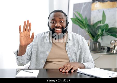 Friendly positive african american man with headset, business leader or coach, conducts business meeting with colleague, discuss ideas and promotion, talks about strategy, records online lesson, smile Stock Photo