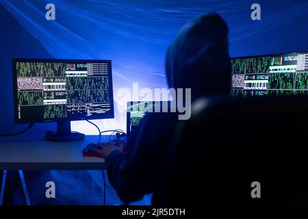Rear view od hooded hacker by computer in the dark room at night, cyberwar concept. Stock Photo