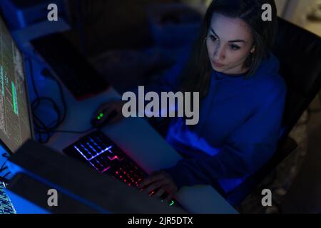 Young woman hacker by computer in the dark room at night, cyberwar concept. Stock Photo