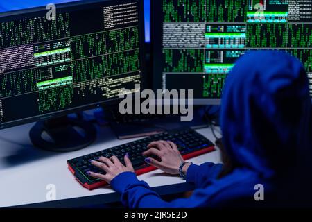 Rear view od hooded hacker by computer in the dark room at night, cyberwar concept. Stock Photo