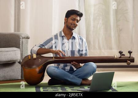 Portrait of young man having online Tanpura lesson Stock Photo