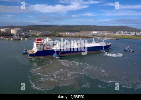 Aerial view of a LNG Tanker cargo ship assisted by tugboats in a port with industrial background. Curtis Island Gladstone Queensland Australia Stock Photo