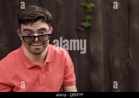 Portrait of happy young man with down syndrome standing outdoors in park and wearing sunglasses Stock Photo