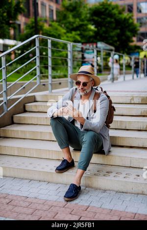 Confident man wearing straw hat and backpack,using phone, businessman in casual clothes in summer on the way to work. Stock Photo