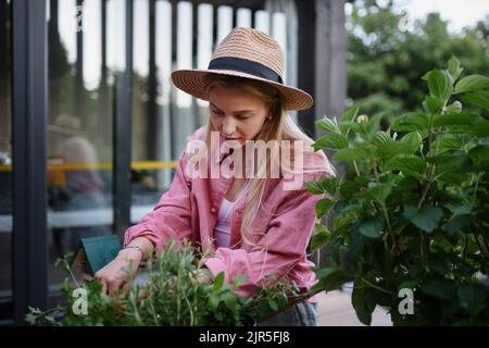 Young woman taking care of her herbs on terrace in tiny house, sustainable living. Stock Photo