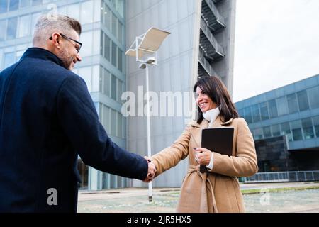 Business man shaking hands with partner in front of office buildings in the city - greeting, dealing, merger and acquisition concepts Stock Photo