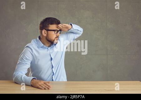 Serious man is sitting at a table and looking into the distance holding his hand over his head. Stock Photo