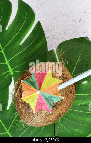 A vertical shot of a coconut on green leaves with a small decorative colorful umbrella on top Stock Photo