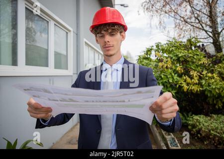 an engineer analyzes a floor plan while he is wearing a protective helmet Stock Photo
