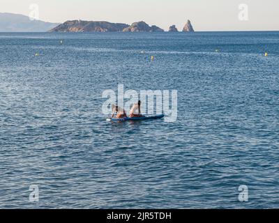 A lovely view of two young women in bikinis with a surfboard floating on the water together Stock Photo