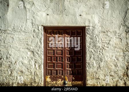 Old and worn maroon double wooden door with a lock on a whitewashed wall very textured by the passage of time Stock Photo