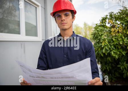An engineer with a floor plan in hand wears a protective case on the construction site Stock Photo
