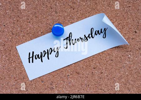 Happy Thursday word on white stick note and pinned to a cork notice board. Stock Photo