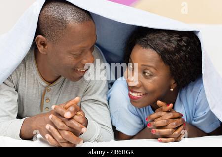 A young couple lying under the cover looks and smiling Stock Photo