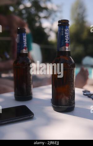 A vertical closeup of two bottles of Belgian Maes Pils beer, and a smartphone on a white table Stock Photo