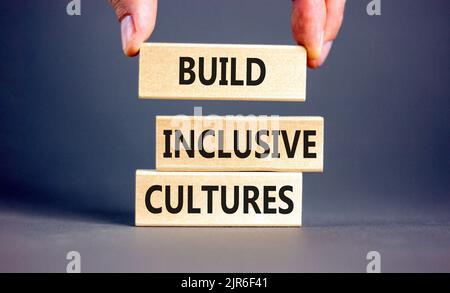 Build inclusive cultures symbol. Concept words Build inclusive cultures on wooden blocks. Businessman hand. Beautiful grey background. Business build Stock Photo