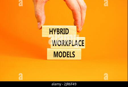 Hybrid workplace models symbol. Concept words Hybrid workplace models on wooden blocks. Businessman hand. Beautiful orange background. Business hybrid Stock Photo