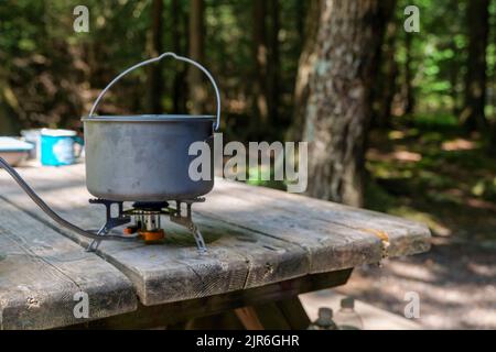 A titanium pot for making food on a gas stove on a camping wooden table in the forest. Stock Photo