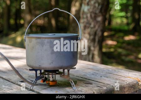 A titanium pot for making food on a gas stove on a camping wooden table in the forest. Stock Photo