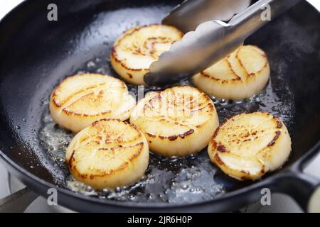 seared scallops in cast iron pan with tongs Stock Photo