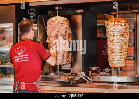 07 July 2022, Antalya, Turkey: chef prepares a doner kebab by cutting toasted slices of meat from the grill spit in a fast food restaurant. Stock Photo