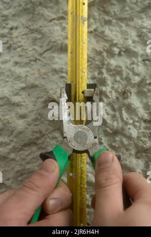 Metal guides for plastering walls, installation of metal beacons on the wall, pliers clamp the beacon holders. Stock Photo
