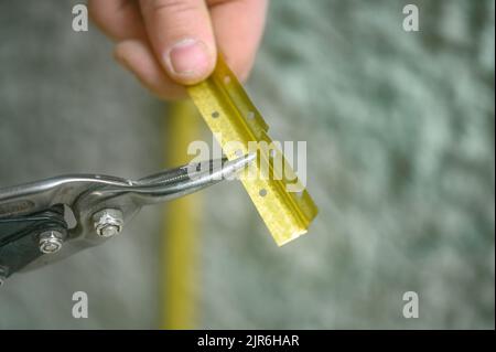 Metal guides for leveling the wall with concrete mortar, installation and fastening of metal guides, the master cuts the guide beacon with scissors. Stock Photo