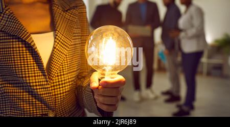 Woman holding bright light bulb as symbol of creative idea, business innovation and success Stock Photo