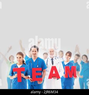 Group portrait of happy medical doctors workers holding TEAM letters on gray background, blue uniform Stock Photo