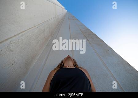 A woman in a black dress looking at the top of a tall building Stock Photo