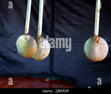 Large kitchen spoons, used in cooking, seen hanging down against a dark background. Stock Photo