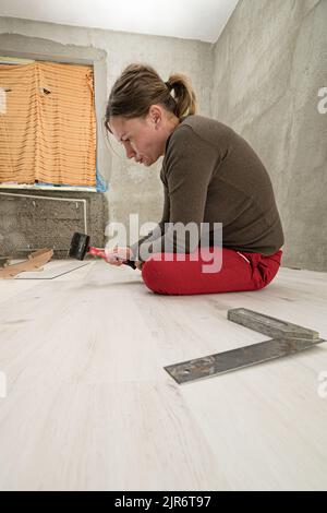 Woman installs quartz vinyl flooring at home, exhausted woman from work Stock Photo