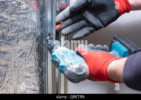 The master screws a metal profile to the wall with a screwdriver, warming the wall near the fireplace with mineral wool and foil. Stock Photo