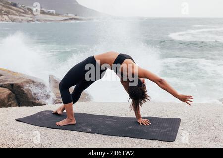 Woman practicing side plank pose by ocean. Young woman doing yoga exercise outdoors. Stock Photo