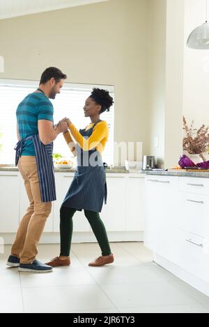 Vertical image of happy diverse couple dancing in kitchen Stock Photo