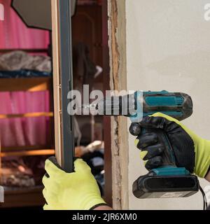 The craftsman drills a hole in the door frame for subsequent attachment to the wall. Stock Photo