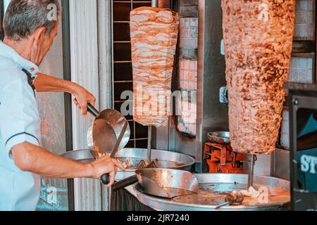 07 July 2022, Antalya, Turkey: chef prepares a doner kebab by cutting toasted slices of meat from the grill spit in a fast food restaurant. Stock Photo