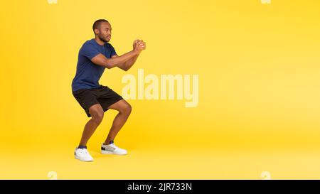 Sporty Black Guy Exercising Doing Deep Squats Over Yellow Background Stock Photo
