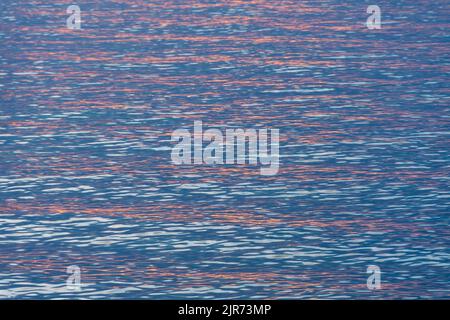 Red reflections of the rising sun at dawn in the calm waters of the Mediterranean Sea. Texture and background for vacation, rest and serenity concepts Stock Photo
