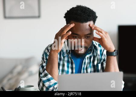 Thoughtful African American Man Using Laptop Working Online Sitting Indoors Stock Photo