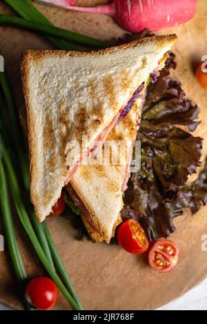 sandwich of two bread toasts with stuffing and vegetables on a wooden board top view Stock Photo