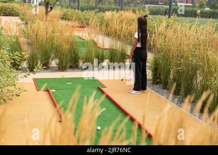 Miniature golf outdoor. Little caucasian girl golfing in the mini golf course. Stock Photo