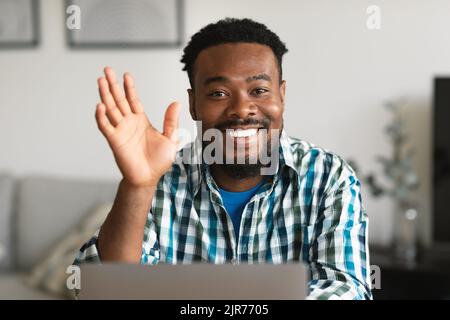 Black Freelancer Guy Waving Hand To Laptop Video Calling Indoor Stock Photo