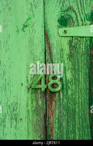 number 48 forty eight on a shabby chic faded green door on a beach hut, green door with number 48 in numerals on the front, number 4 and 8 four eight. Stock Photo