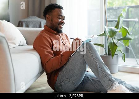 Cheerful Black Male Writing Taking Notes Sitting At Home Stock Photo